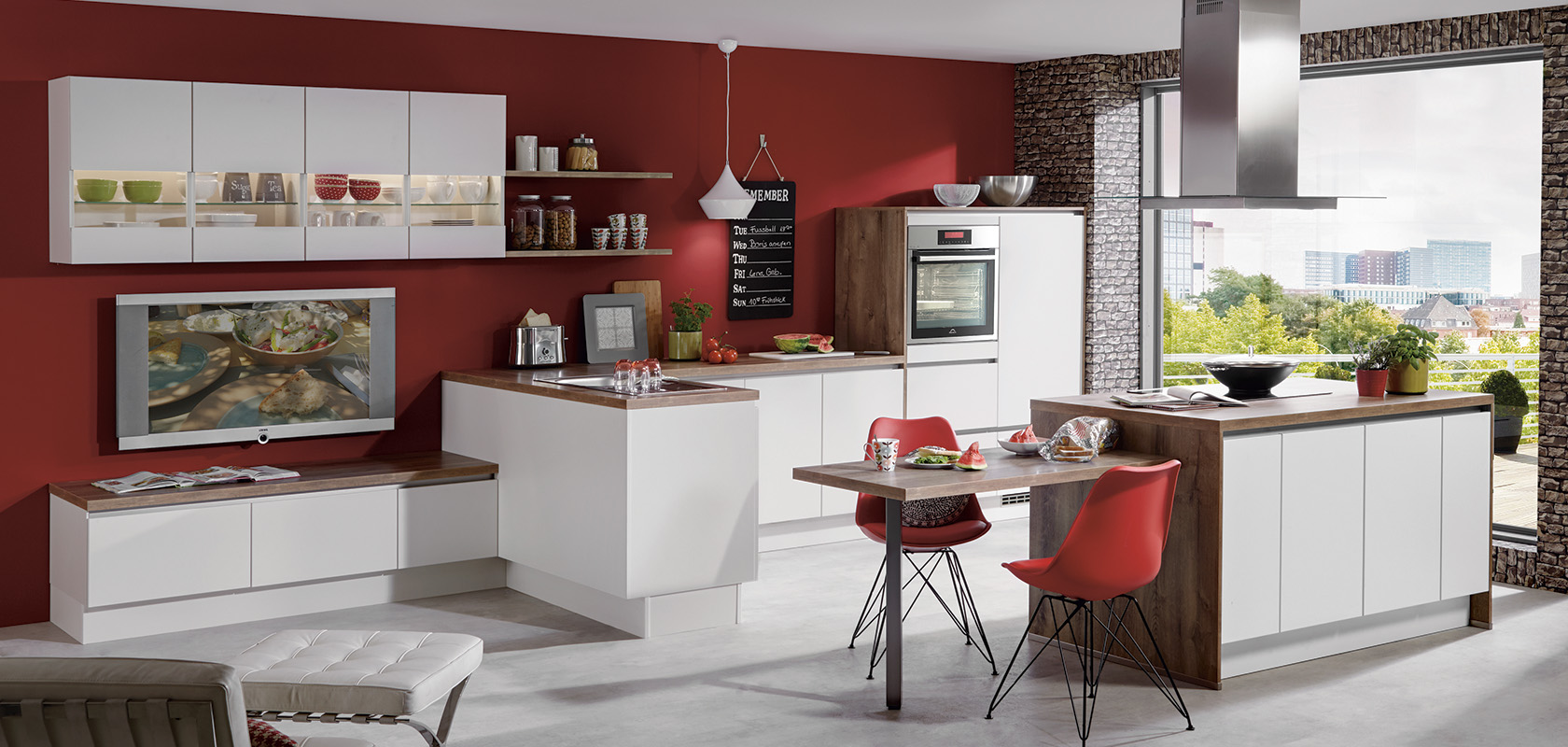 Modern kitchen interior with white modular cabinetry, red accent walls, brick features, sleek appliances, and a cozy dining area with a picturesque window view.