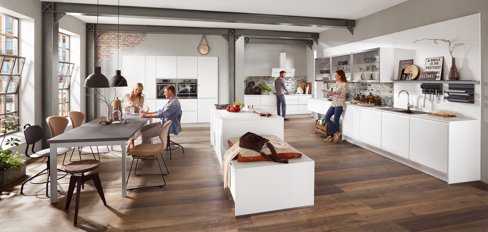 Spacious modern kitchen with a dining area showcasing lively friends enjoying a meal, with natural light enhancing the contemporary interior design.