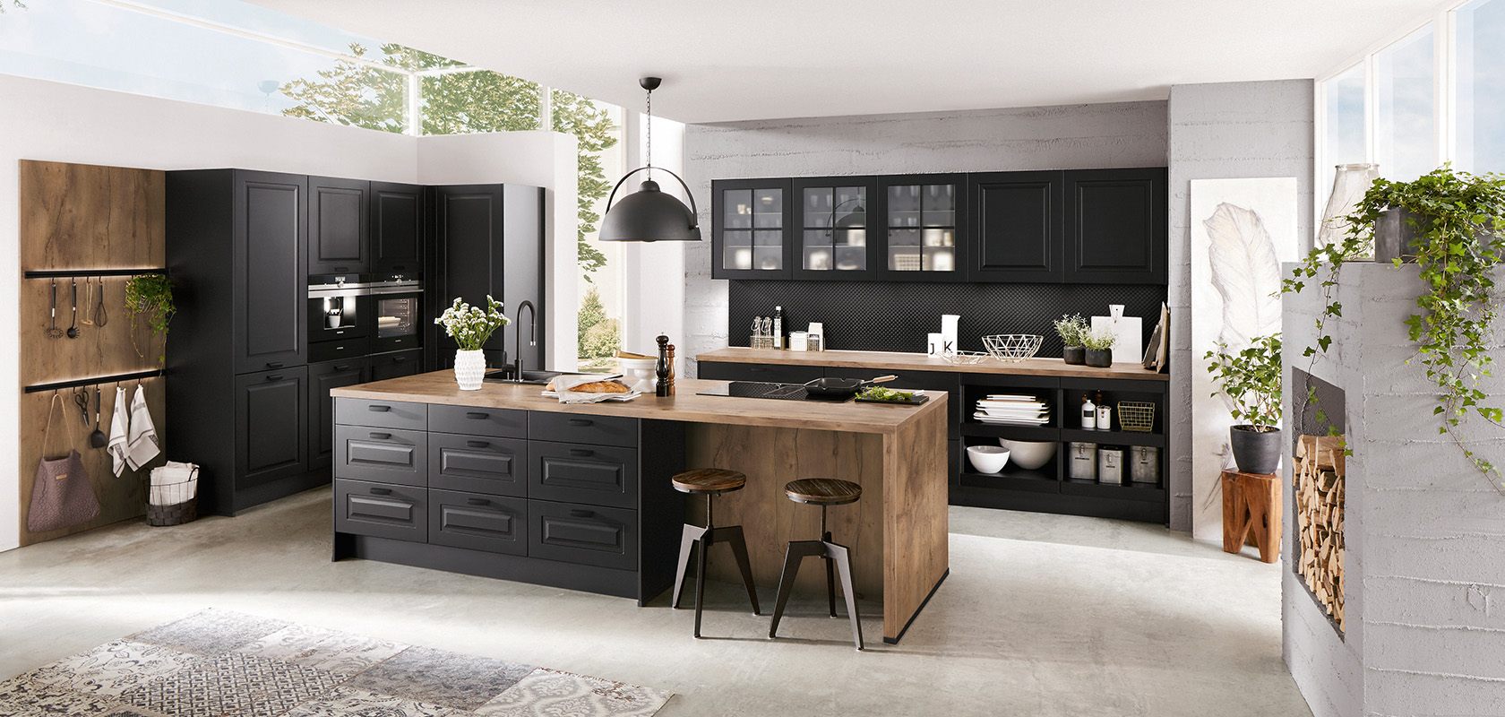 Interni di cucina moderna che mostrano eleganti armadi neri, dettagli in legno e un'isola centrale, arricchiti da luce naturale e verde per uno spazio elegante e accogliente.