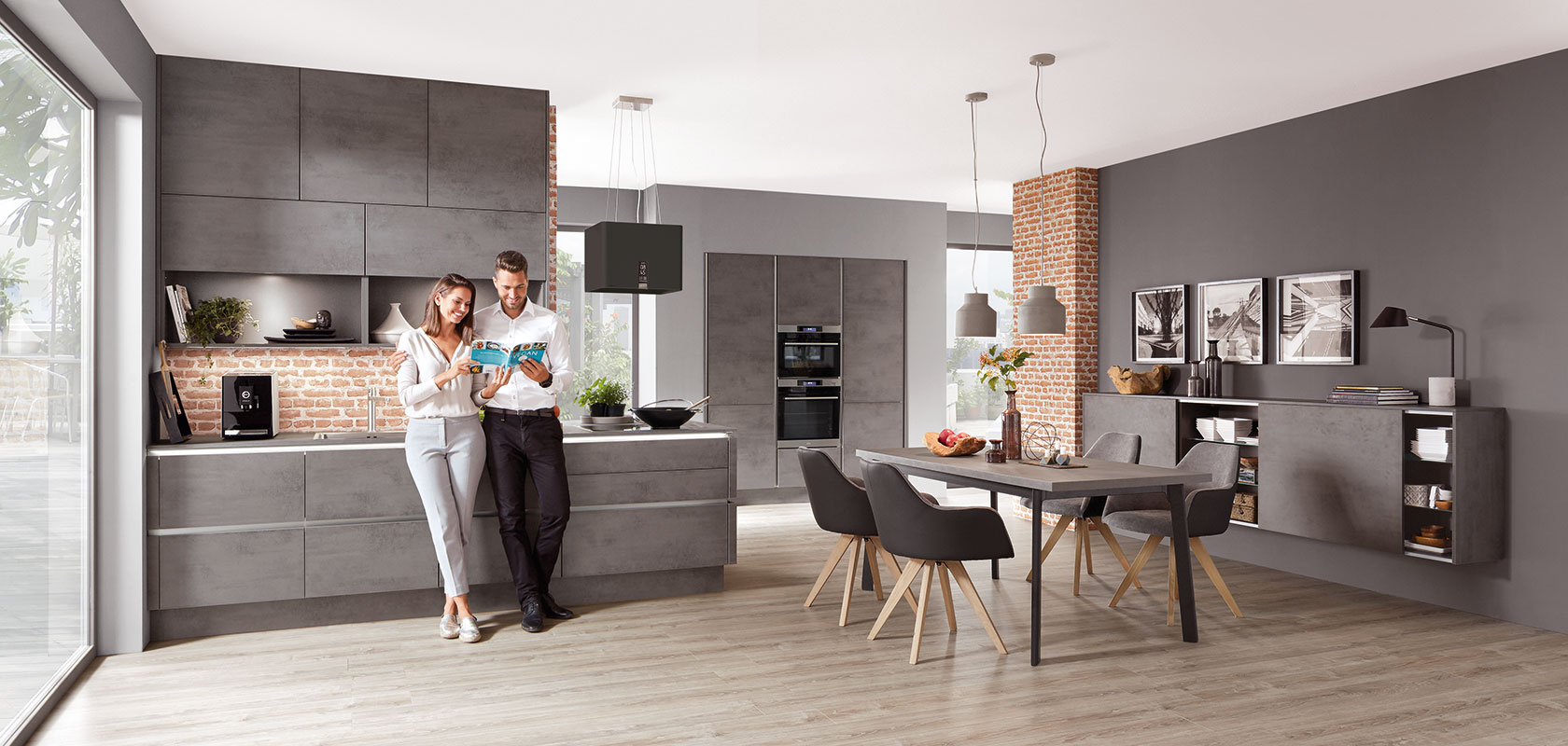 A stylish, modern kitchen with a couple enjoying coffee, featuring sleek gray cabinetry, exposed brick, and a spacious dining area with contemporary decor.