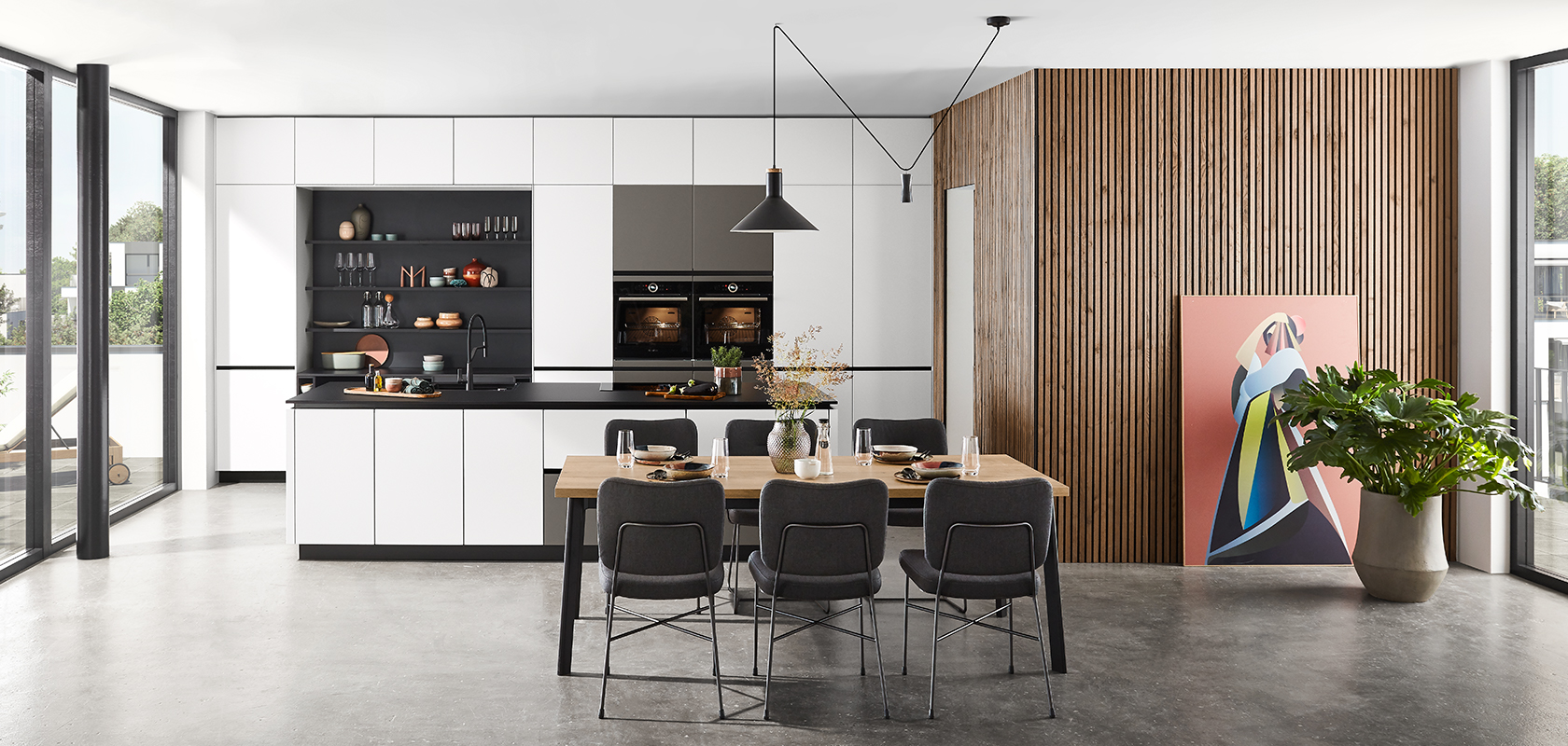 Moderne keukeninterieur met strakke zwarte en witte kasten, houten accenten en een eethoek met stijlvol meubilair onder elegante hanglampen.