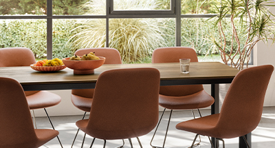 Espace repas élégant avec une table en bois lisse accompagnée de chaises en terre cuite, une lumière naturelle et des plantes vertes qui rehaussent une ambiance moderne et sereine à la maison.