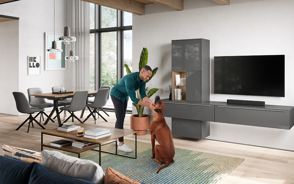 Un salon moderne avec un homme en tenue décontractée interagissant joyeusement avec son chien, entouré de meubles élégants et d'une décoration contemporaine.