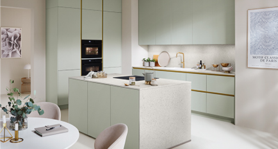Elegante diseño de cocina moderna con gabinetes verdes tenues, acentos dorados, electrodomésticos integrados y decoración minimalista, mostrando un espacio de vida elegante pero funcional.