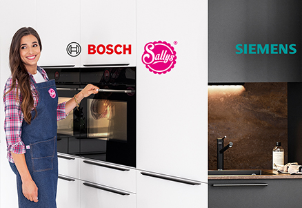 Lachende vrouw in een schort presenteert strakke Bosch en Siemens ovens in een moderne keuken, ter promotie van Sally's samenwerking met topapparatenmerken.