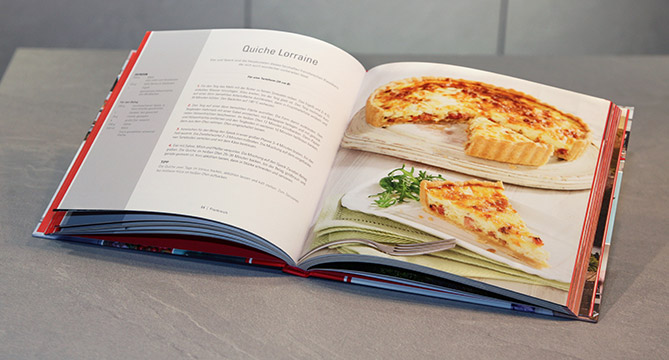 An open cookbook on a kitchen counter displaying a vibrant, appetizing image and recipe for Quiche Lorraine, inviting culinary exploration.