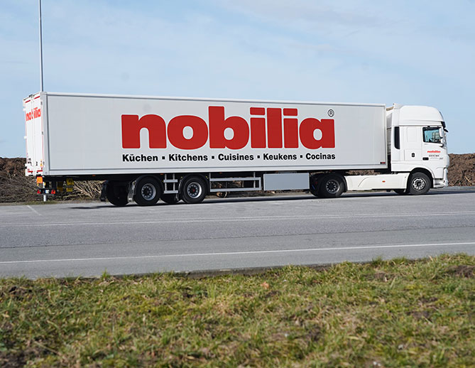 Un camión de la marca nobilia en la carretera, anunciando cocinas en varios idiomas, simbolizando la entrega internacional de muebles y suministros de cocina.