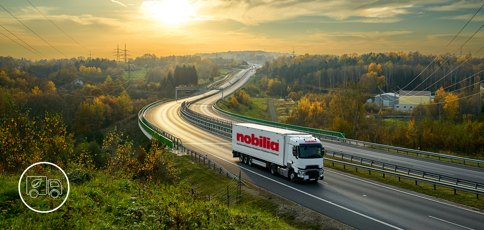 Un camión comercial de la marca "nobilia" viaja por una carretera sinuosa en medio de un vibrante paisaje otoñal con follaje y colinas ondulantes a lo lejos.