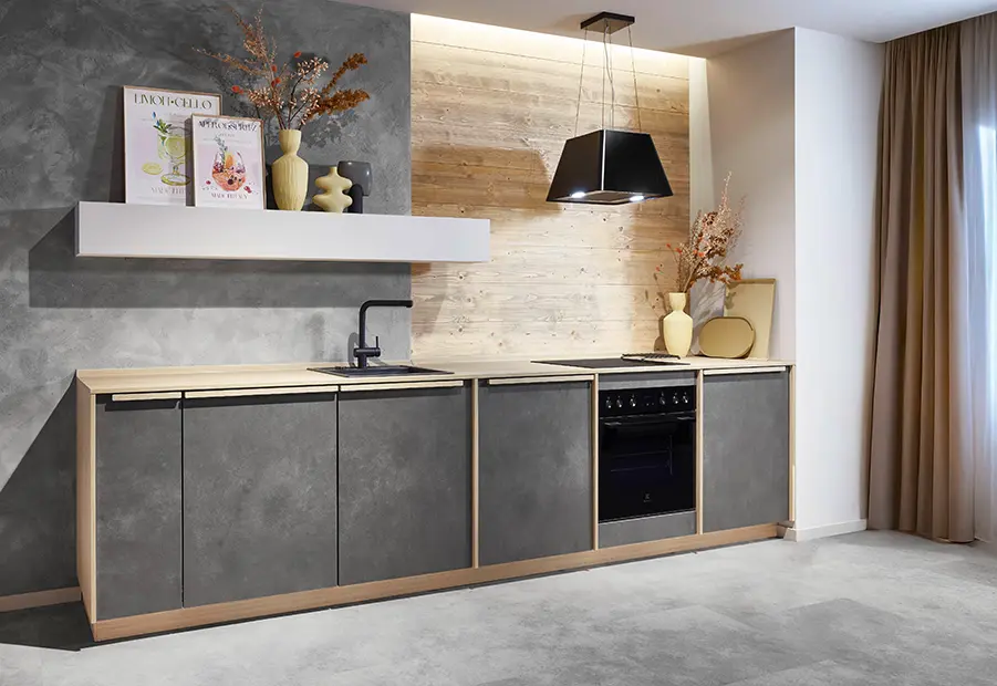 Einzeilige Küche mit grauen Fronten in Beton-Optik und sichtbaren Holzkanten, darüber eine schwarze Dunstabzugshaube und ein offenes Wandboard.