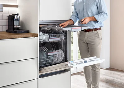 [Translate to it:] Geöffneter Geschirrspüler in moderner Einbauküche. Der Oberkorb wird bequem beladen. Elegantes Küchendesign mit integrierter Spülmaschine auf ergonomischer Höhe.