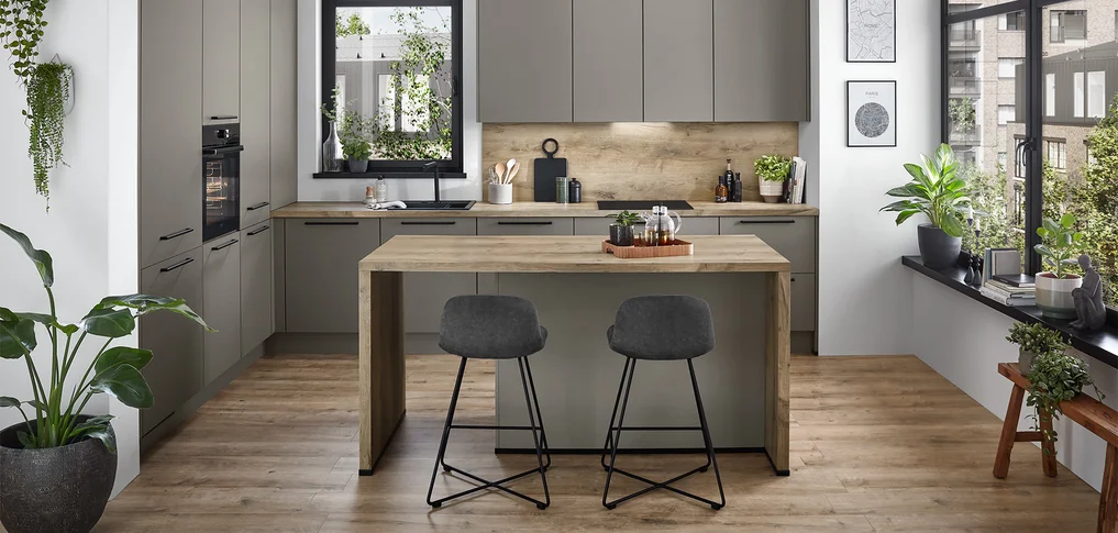 Cette cuisine présente la **Front Laser 461** dans la couleur **Gris taupe** - un ton chaud et terreux qui est à la fois intemporel et confortable. La combinaison avec un plan de travail en bois et un habillage de crédence assorti apporte du naturel et de la chaleur à la pièce. Les poignées foncées créent des contrastes discrets et soulignent le look moderne de cette cuisine habitable accueillante. Idéal pour tous ceux qui souhaitent allier élégance sobre et atmosphère conviviale.