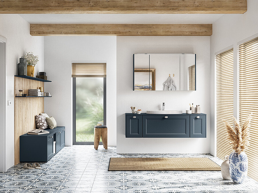 Modernes Badezimmerinterieur mit einem blauen Waschtischschrank, Spiegel, Holzakzenten und gemusterten Bodenfliesen, das eine ruhige und stilvolle Atmosphäre vermittelt.