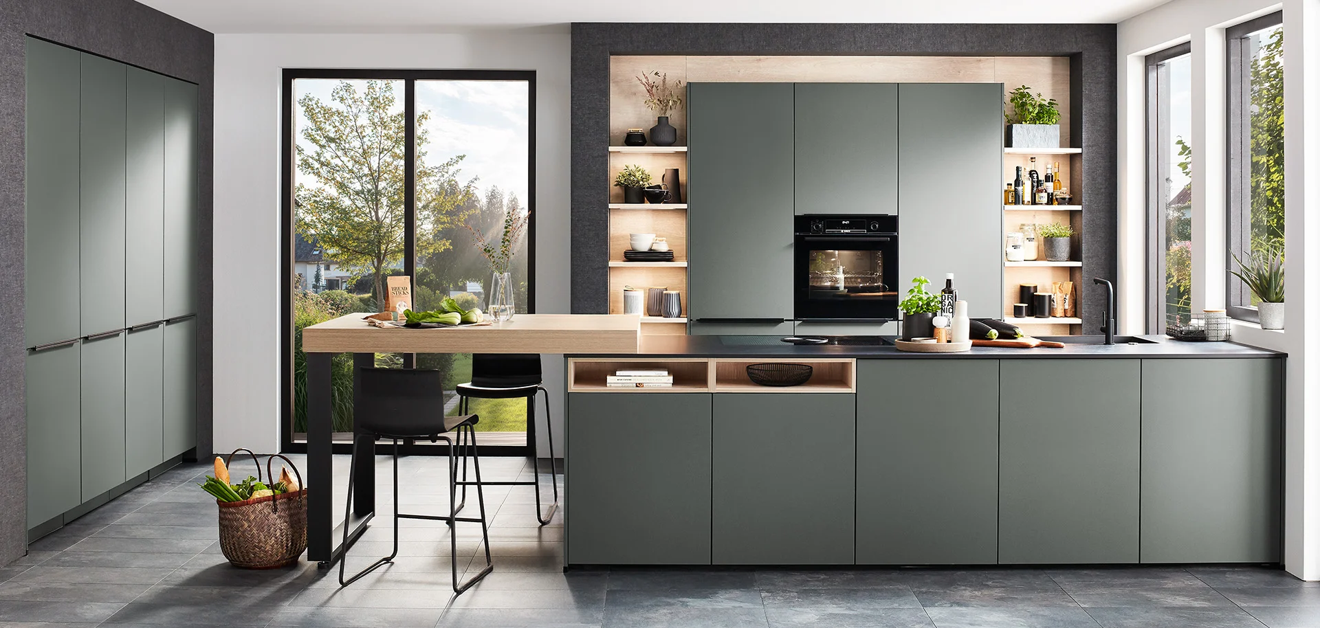 Nowoczesne wnętrze kuchni z eleganckimi zielonymi szafkami, zintegrowanymi urządzeniami AGD i płytą indukcyjną na ciemnym blacie, emanujące współczesnym stylem i funkcjonalnością.