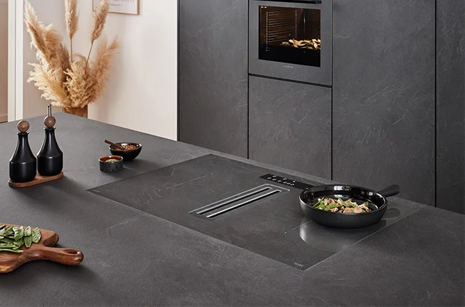 [Translate to pl:] nobilia Xtra Hob Kochfeld mit integriertem Dunstabzug in Grauschiefer Nachbildung 303 – flächenbündig in Arbeitsplatte und Küchenfront Stoneart 303 integriert – einheitliches Design mit unsichtbarer Technik – modernes Küchenambiente mit passendem Backofen in gleicher Farbe