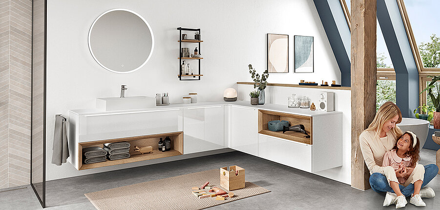 Intérieur de salle de bain moderne avec une élégante vanité blanche, un miroir circulaire et une mère interagissant joyeusement avec son enfant sur un sol chaud et ensoleillé.