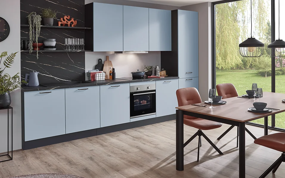 Nowoczesna kuchnia z frontem SENSO 485 w matowym kolorze Sky Premium w połączeniu z czarnym marmurem na ścianie i przytulną jadalnią z widokiem na zieleń.