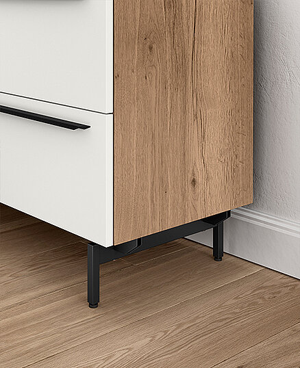 Modern two-tone cabinet with a white drawer and wood veneer door, featuring sleek black handles and legs, on a herringbone parquet floor.