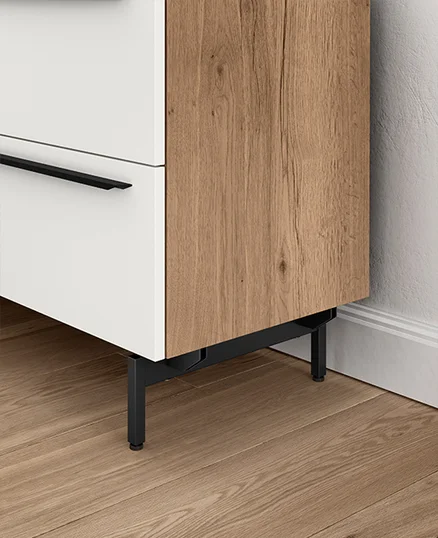 Gabinete moderno de dos tonos con un cajón blanco y una puerta de chapa de madera, con elegantes manijas y patas negras, sobre un piso de parquet en espiga.