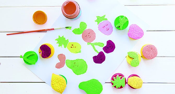 Colorful sponge painting activity for children on a white surface, with paint pots and brushes, promoting creativity and fun with art.