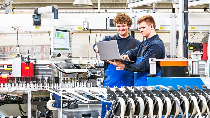 Auszubildende als Mechatroniker in der Produktion analysieren Maschinendaten und optimieren Fertigungsprozesse mit moderner Technik.