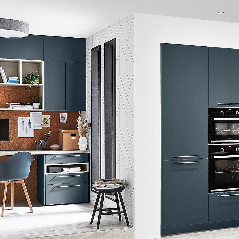 Stilvolle Home-Office-Ecke in einer Küche mit einem zeitgenössischen Schreibtisch, Regalen und minimalistischen Schränken in einem abgestimmten blauen und Holz-Finish.