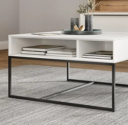 Mesa de café blanca minimalista con patas de metal negro elegantes, que cuenta con un estante abierto con libros y objetos decorativos, en un espacio de vida moderno.