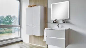 Bad mit Griffmuldenbeleuchtung am Waschtischunterschrank und beleuchtetem Spiegel in hellem Design.