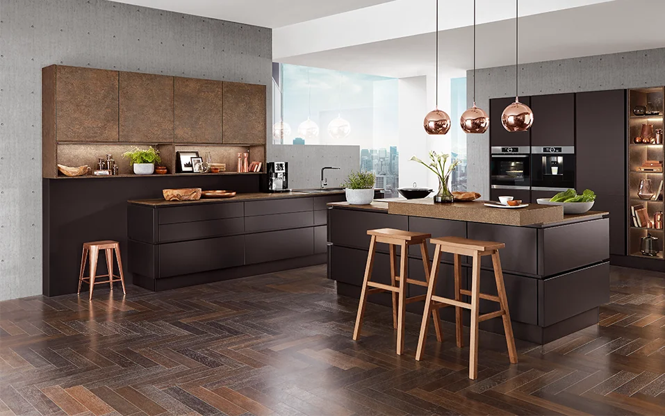 El frente TOUCH 340 en negro supermate confiere a esta cocina un aspecto llamativo a la par que elegante. La superficie mate tiene un aspecto especialmente moderno y es agradablemente fácil de limpiar. Combinada con cálidos tonos cobrizos y detalles de madera, crea un elegante concepto de vida con mucha profundidad y carácter.