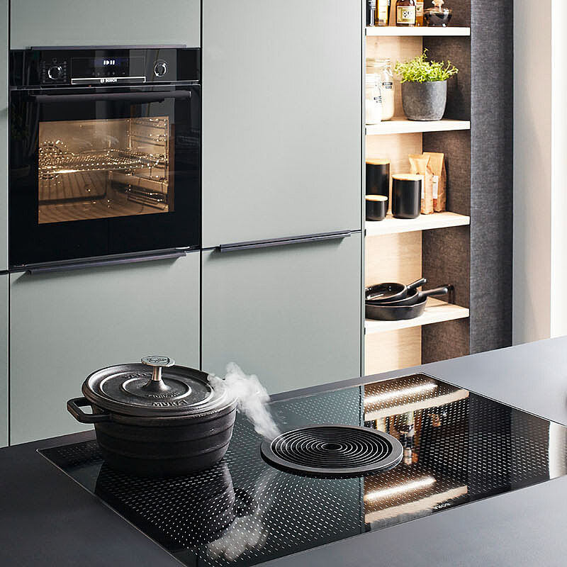 Nowoczesne wnętrze kuchni z eleganckimi zielonymi szafkami, zintegrowanymi urządzeniami AGD i płytą indukcyjną na ciemnym blacie, emanujące współczesnym stylem i funkcjonalnością.