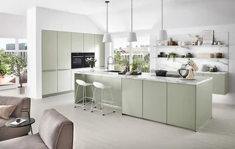 Cucina senza maniglie di colore chiaro con frontale SENSO 494 in Jade Premium opaco, isola di cottura con piano di lavoro in marmo e ripiani aperti davanti a un'ampia finestra frontale nel soggiorno moderno.