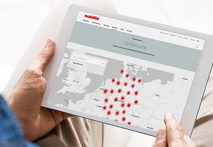 Osoba drží tablet s otevřeným vyhledávačem prodejců Nobilia a mapou plnou umístění.