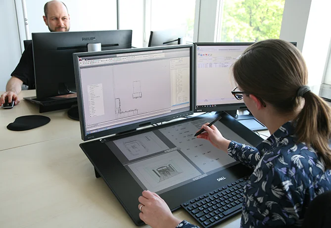 Zwei Fachleute arbeiten in einem Büro mit Computern und konzentrieren sich auf eine grafische Designaufgabe auf einem digitalen Zeichentablett.