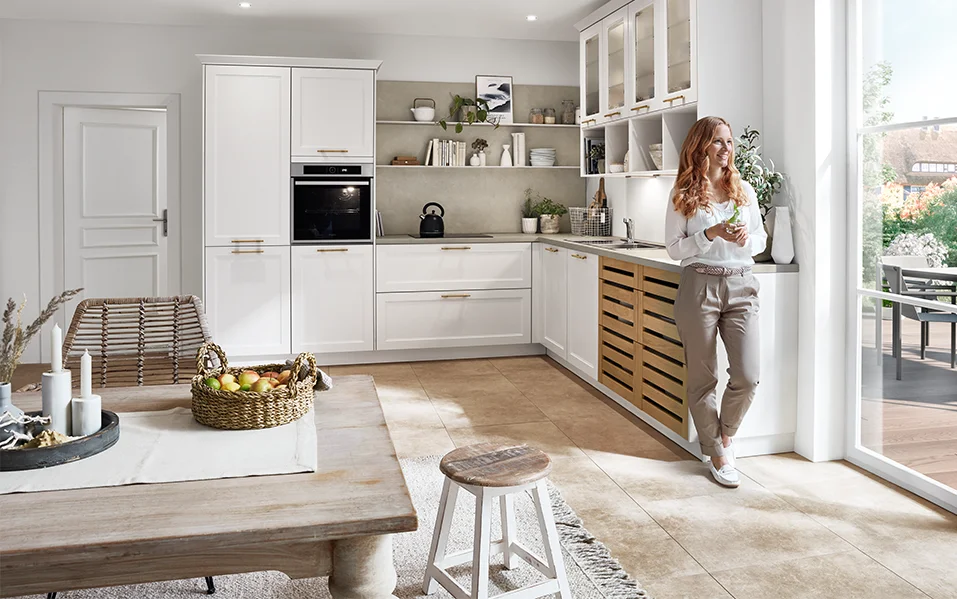 Bright country-style kitchen with CASCADA 774 front in white, combined with wooden details and golden handles, open design with plenty of natural light.