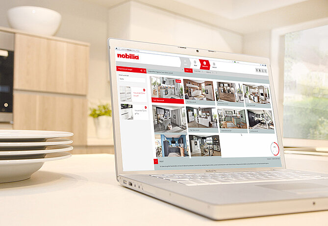 Laptop na blacie kuchennym wyświetlający stronę internetową z galerią nowoczesnych projektów wnętrz, prezentujących markę Nobilia.