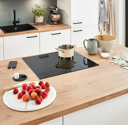 Cocina moderna con encimera de madera, una olla sobre la placa de cocción y fruta fresca en un plato de mármol.
