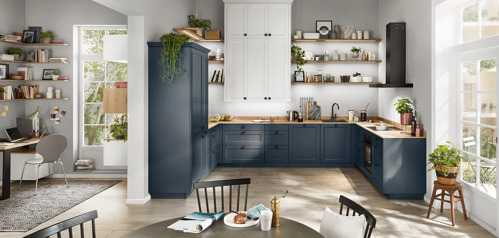 Cucina moderna da casa di campagna con piano cottura e zona cottura in nobilia Cascada 778 front in blu fiordo. La cucina offre un'elegante combinazione di basi blu, scaffali aperti, pensili bianchi e una postazione di lavoro integrata.