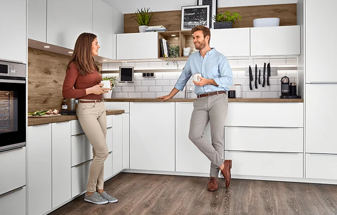 Eine Frau in einer modernen Küche lädt den Geschirrspüler und betont die eleganten, eingebauten Geräte und das minimalistische Dekor in einem hellen, luftigen Raum.