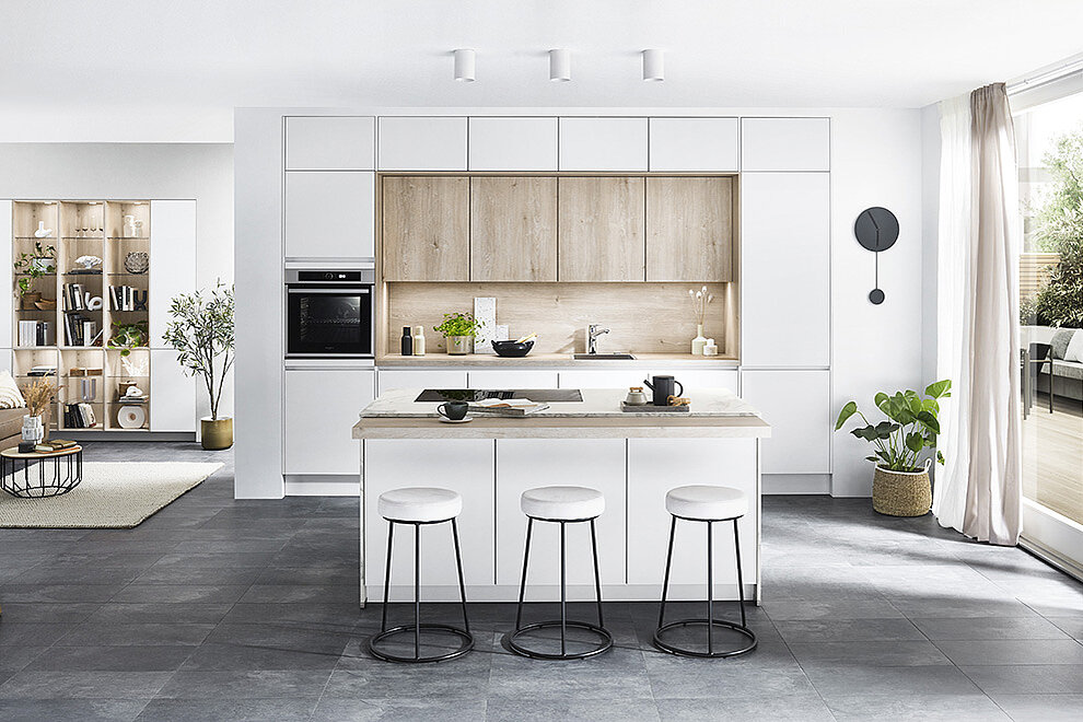 Elegante moderne keuken met strakke witte kasten, houten accenten en een centraal eiland met barkrukken in een lichte, ruime kamer.