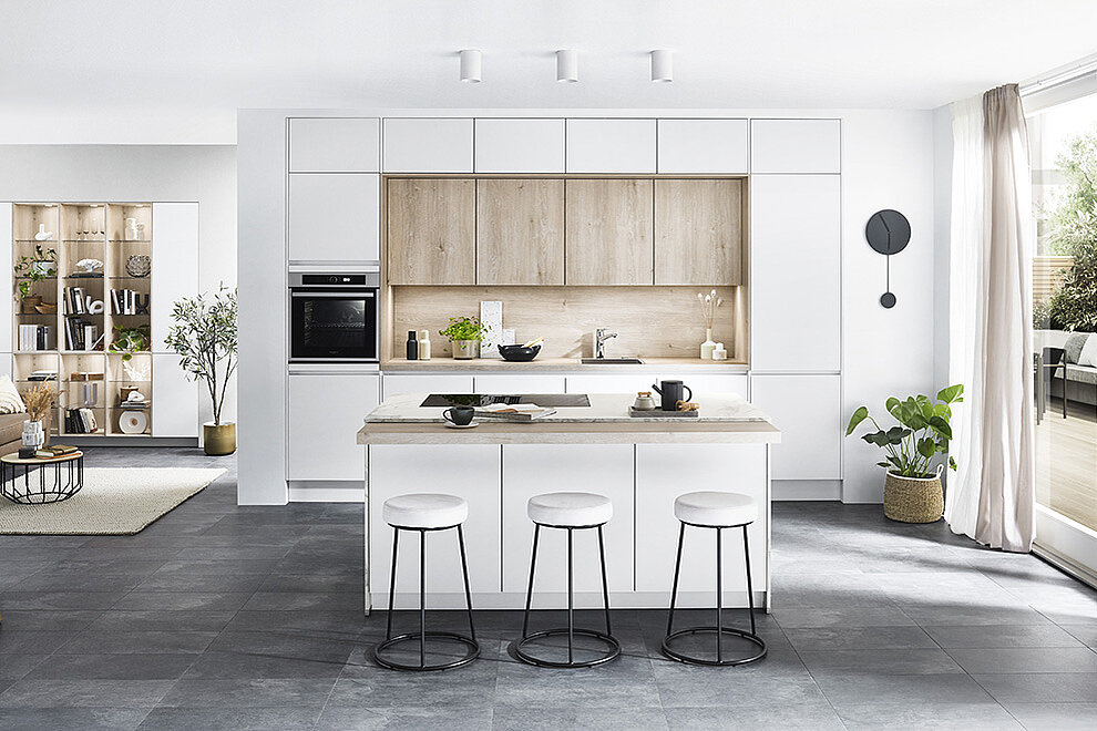 Elegant modern kitchen with clean white cabinetry, wooden accents, and a central island with bar stools set in a bright, spacious room.