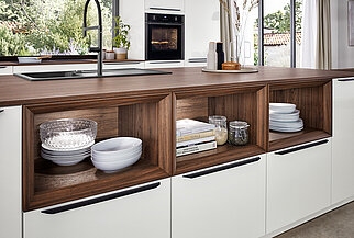 A stylish kitchen featuring white cabinets with dark wood detailing, organized shelving, and integrated appliances, highlighting a blend of modern design and practicality.