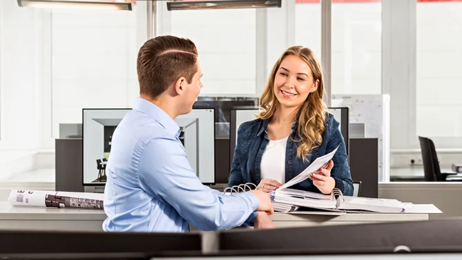 Auszubildende zur Industriekauffrau und ihr Kollege besprechen Unterlagen in einem modernen Büro – kaufmännische Ausbildung mit Schwerpunkt Verwaltung und Organisation.