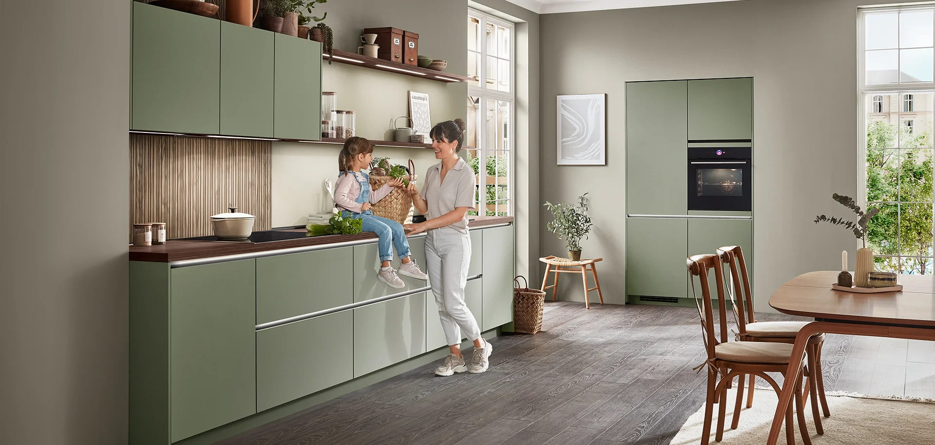 nobilia SENSO Küche mit grünen Fronten und recycelter Melaminspanplatte sowie Frau und Kind an der Küchenzeile