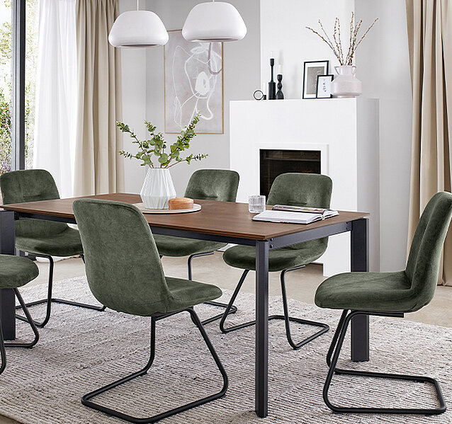 Elegantní jídelna s tmavým dřevěným stolem, plyšovými zelenými židlemi a minimalistickým dekorem s elegantním bílým krbem a jemnými neutrálními tóny.