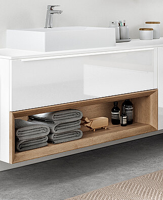 Modern bathroom vanity with white countertop, integrated sink, and wooden lower shelf stocked with towels and toiletries in a minimalistic design.