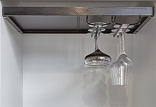 Blick von unten auf eine moderne Küche, die einen Edelstahl-Weinglashalter mit zwei hängenden Weingläsern zeigt, vor einem sauberen, neutralen Hintergrund.