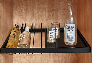 Un estante minimalista con elegantes botellas de tocador y una botella de agua transparente decorativa, situado contra un cálido fondo de madera.
