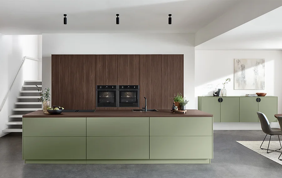 Nowoczesna kuchnia z frontem SENSO 495 w matowym kolorze Olive Premium w połączeniu z boazerią z ciemnego drewna i dużą wyspą kuchenną w harmonijnym wystroju wnętrza.