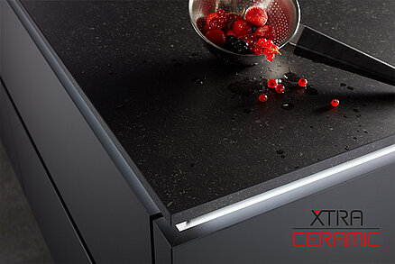 Piano cottura a induzione XTRA CERAMIC moderno con un design elegante e bacche sparse che aggiungono un tocco di colore alla sofisticata superficie scura.