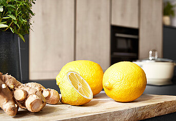 Des citrons frais et une racine de gingembre sur une planche à découper en bois, suggérant des ingrédients sains dans un cadre de cuisine moderne.