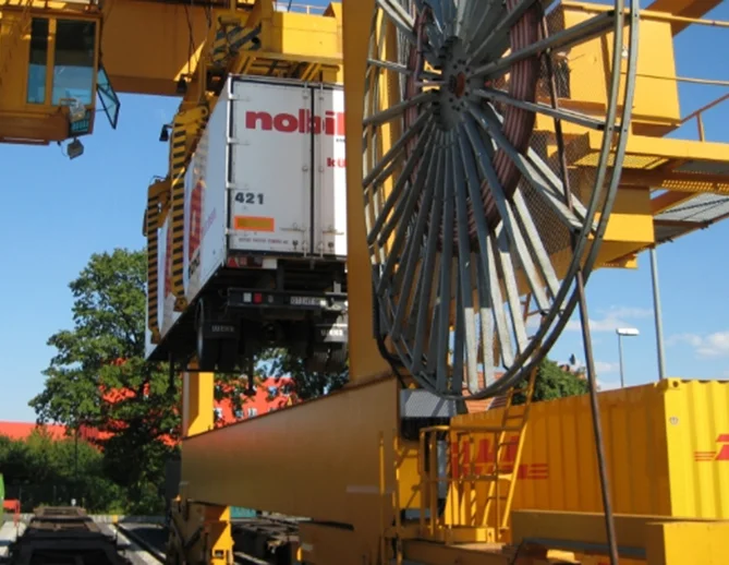 Una gran grúa levantando un contenedor de carga comercial contra un cielo azul claro, mostrando equipos industriales y capacidades logísticas.